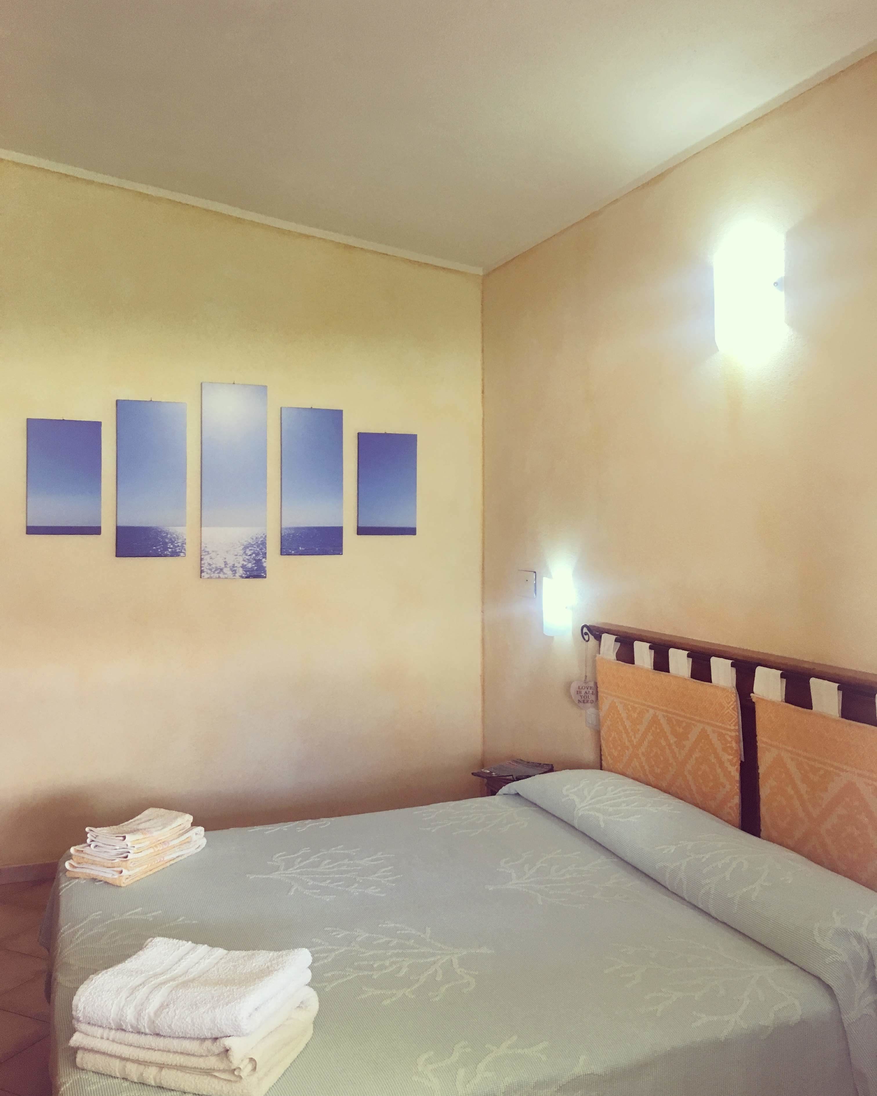 A hotel room with a bed, a wall-mounted artwork, a bedside table, and a lamp.