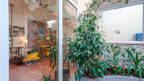 A room with a glass door leading to a space with a yellow scooter, a lamp, and a bookshelf.
