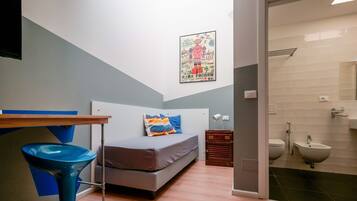 Ein kleiner, moderner Raum mit einem Bett, einem blauen Stuhl, einem kleinen Tisch und einem Badezimmer mit Toilette und Waschbecken.