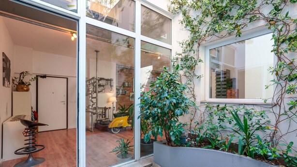 A modern interior with large glass doors leading to a living area, a compact kitchen, and a small balcony with plants.