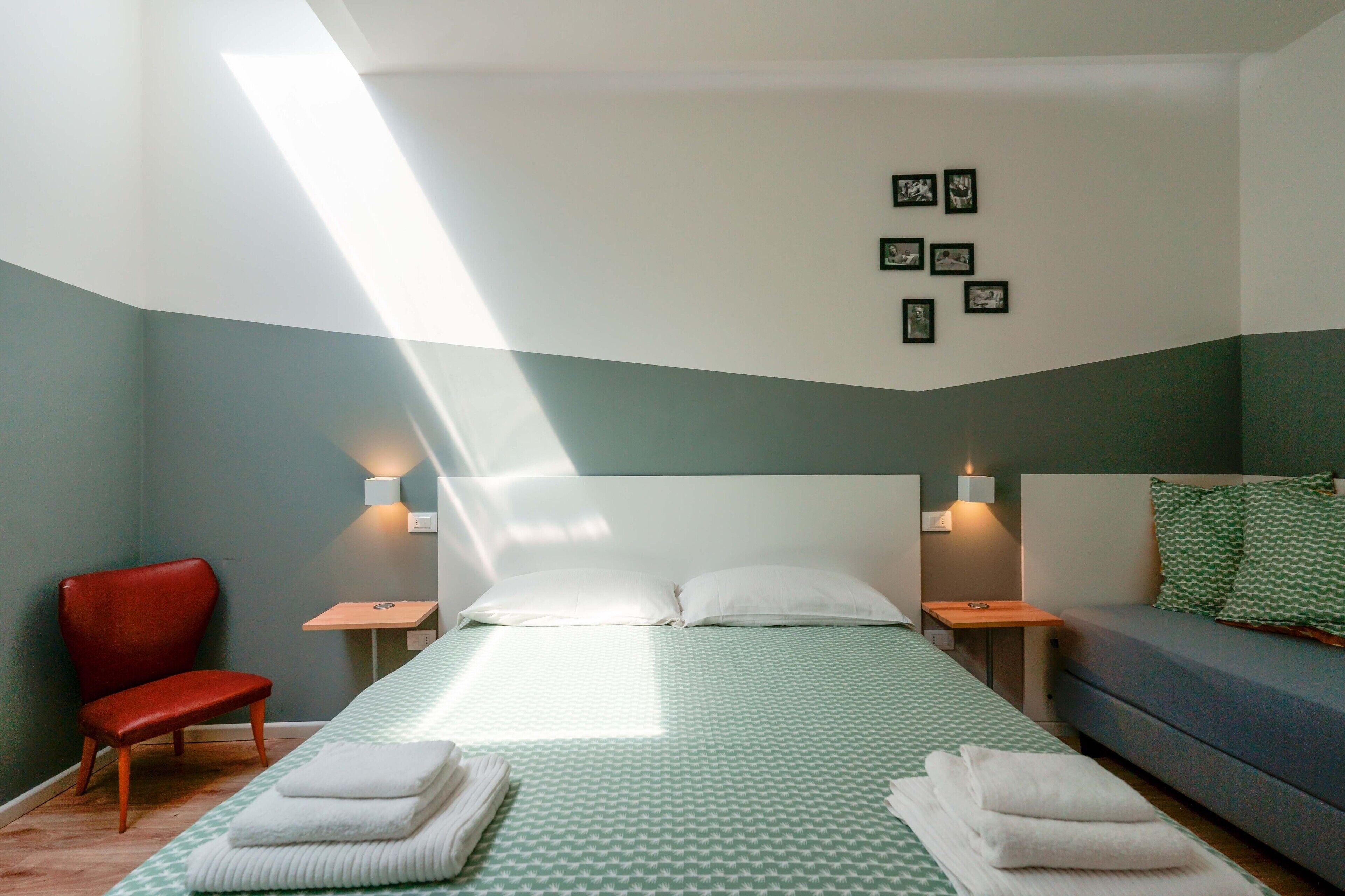 Une chambre à coucher avec un lit, un fauteuil rouge, un canapé et des lampes fixées au mur.