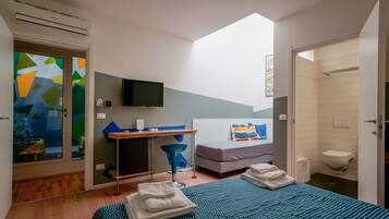 A modern bedroom with a skylight, a desk, a bed with blue bedding, and a shower area.