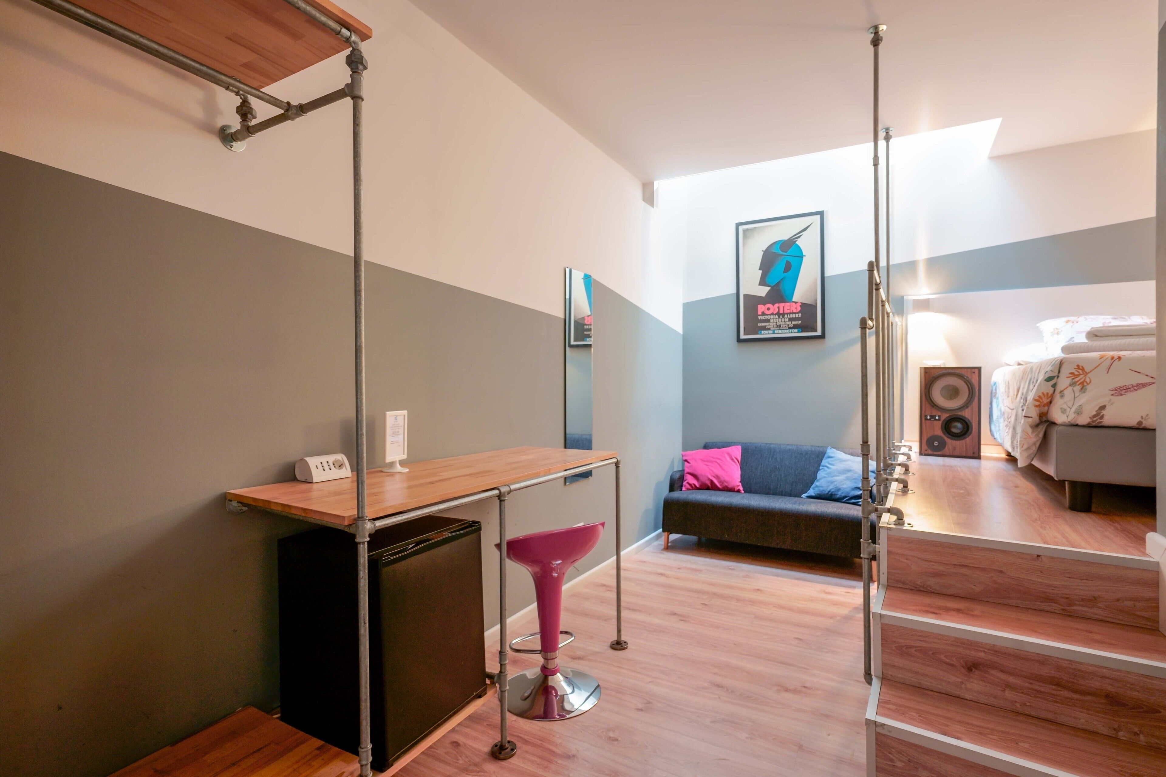 Una habitación moderna con un escritorio de madera, una silla rosa, un sofá y una cama.