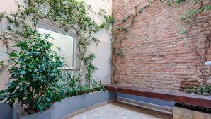 A courtyard with a brick wall, a window, and a planter with plants.