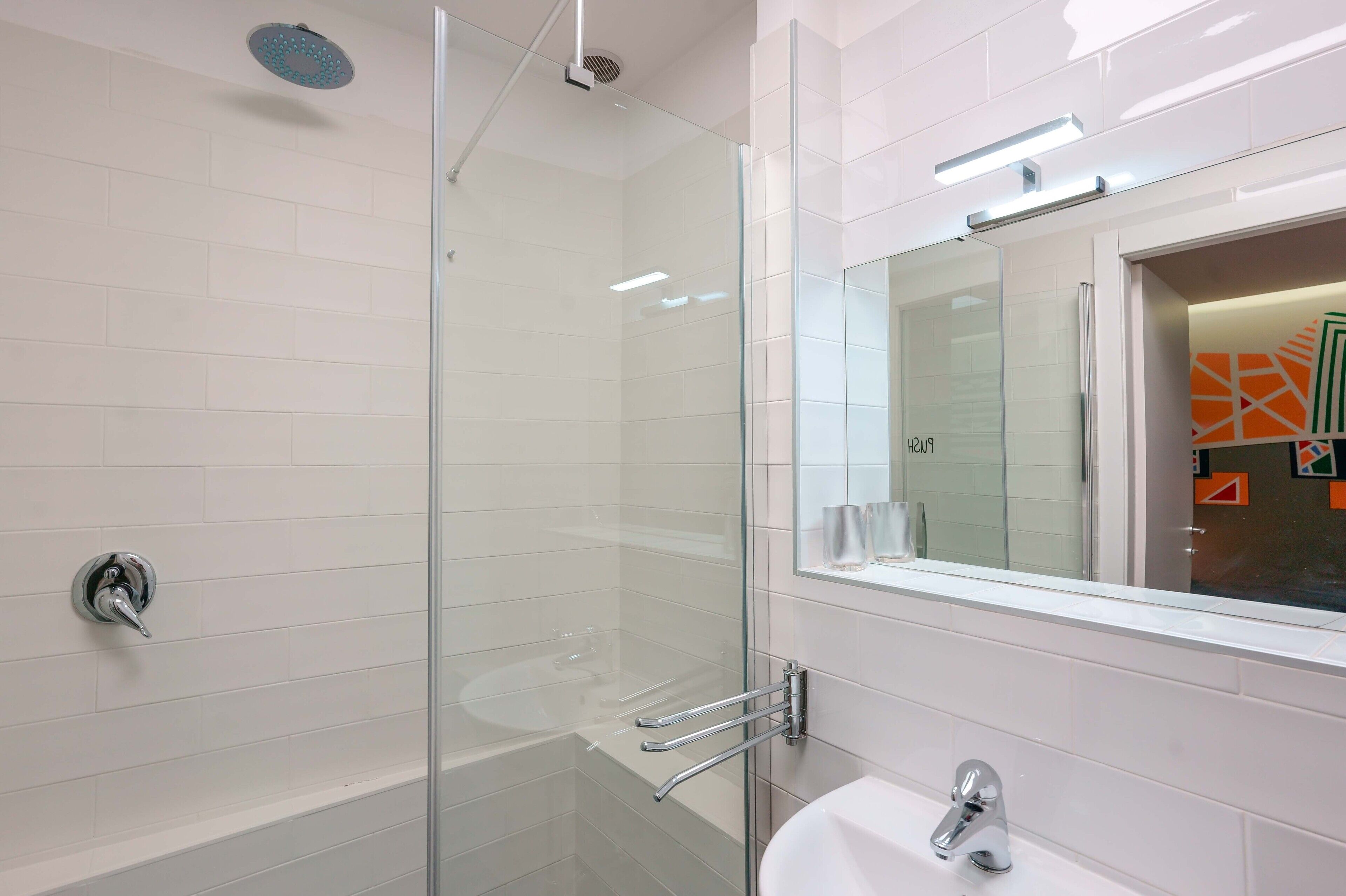 Un bany modern amb plat de dutxa de vidre, un lavabo blanc i un mirall amb marc decoratiu.