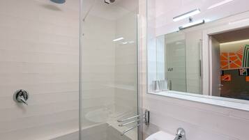 Un bany modern amb plat de dutxa de vidre, un lavabo blanc i un mirall amb marc decoratiu.