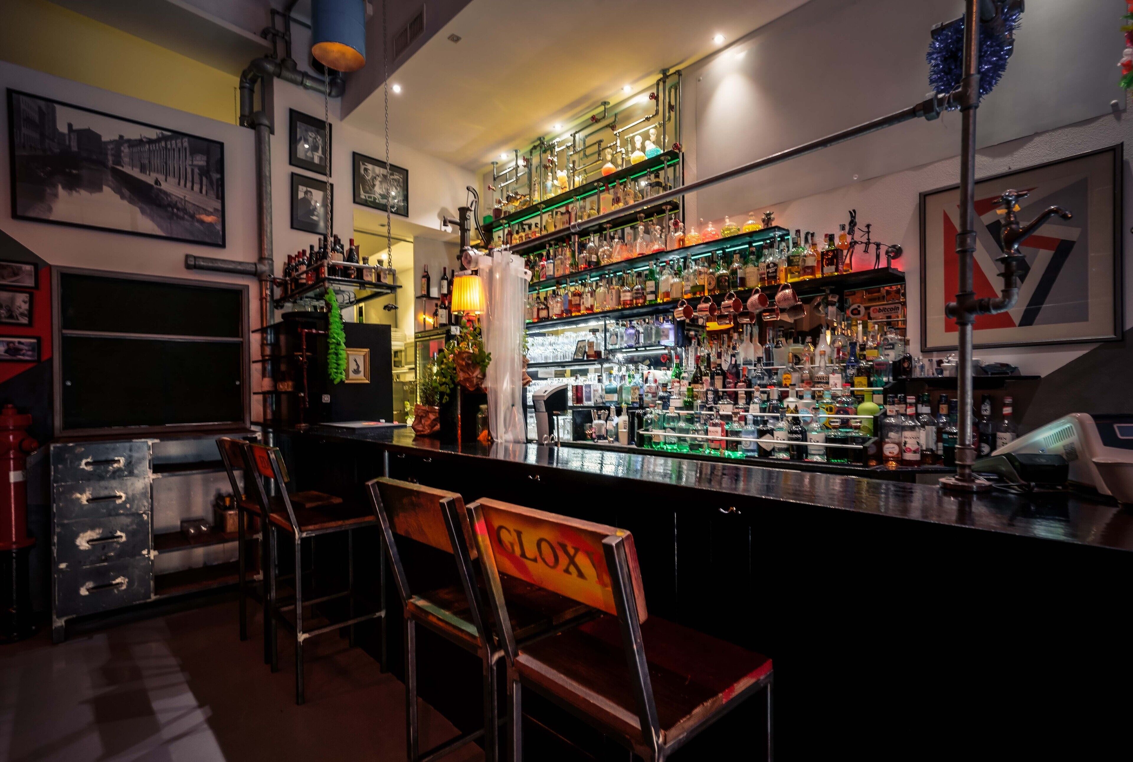 A bar area with a variety of liquor bottles, a bar counter, and two chairs with a sign.