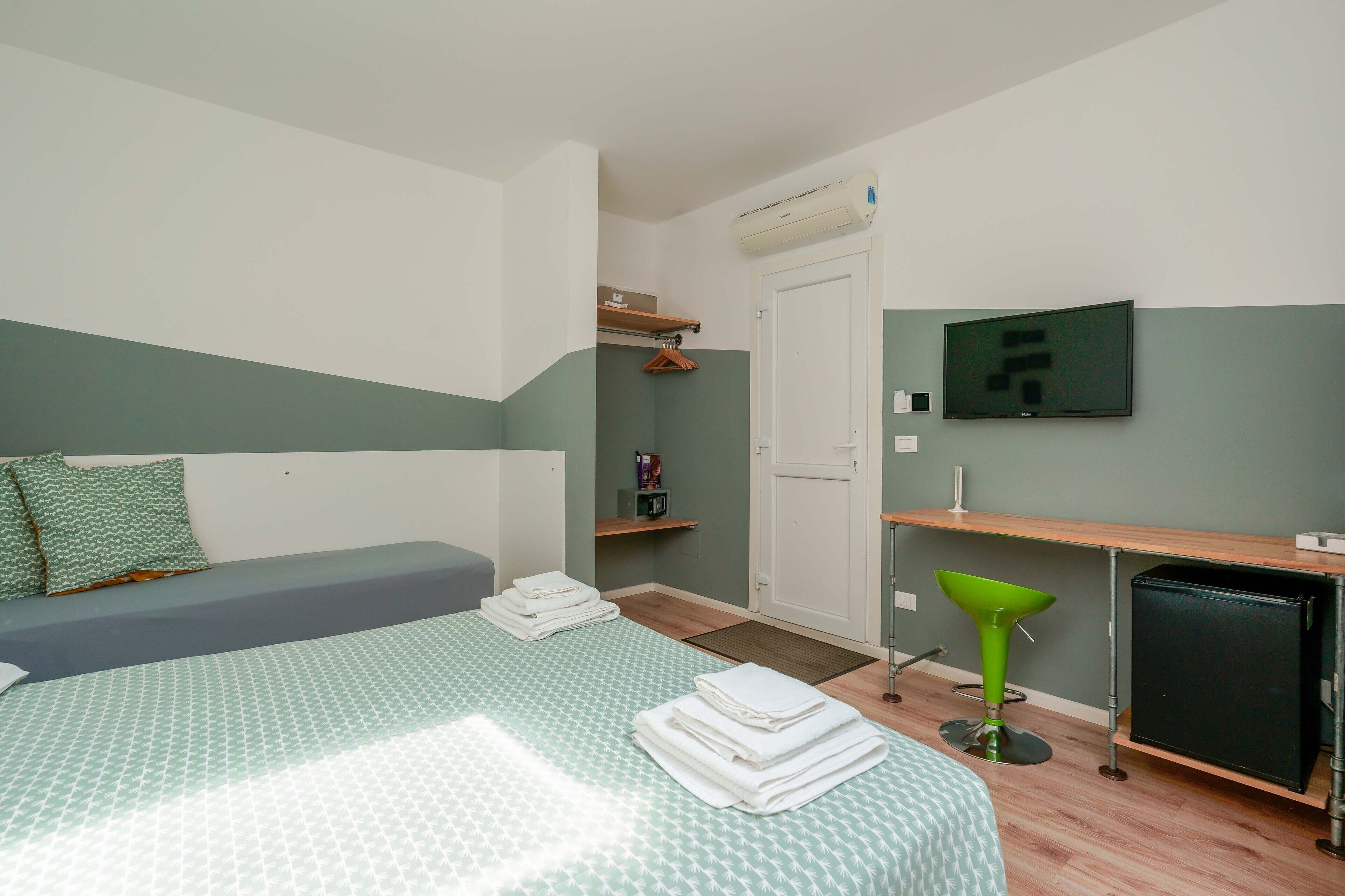 Een slaapkamer met een bed, een bureau, een stoel, een televisie en een kleine koelkast.