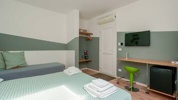 Een slaapkamer met een bed, een bureau, een stoel, een televisie en een kleine koelkast.