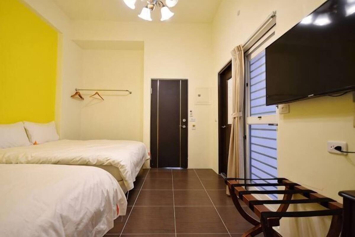 Ein Hotelzimmer mit zwei Betten, einem Fernseher, einer Tür und einem Fenster.