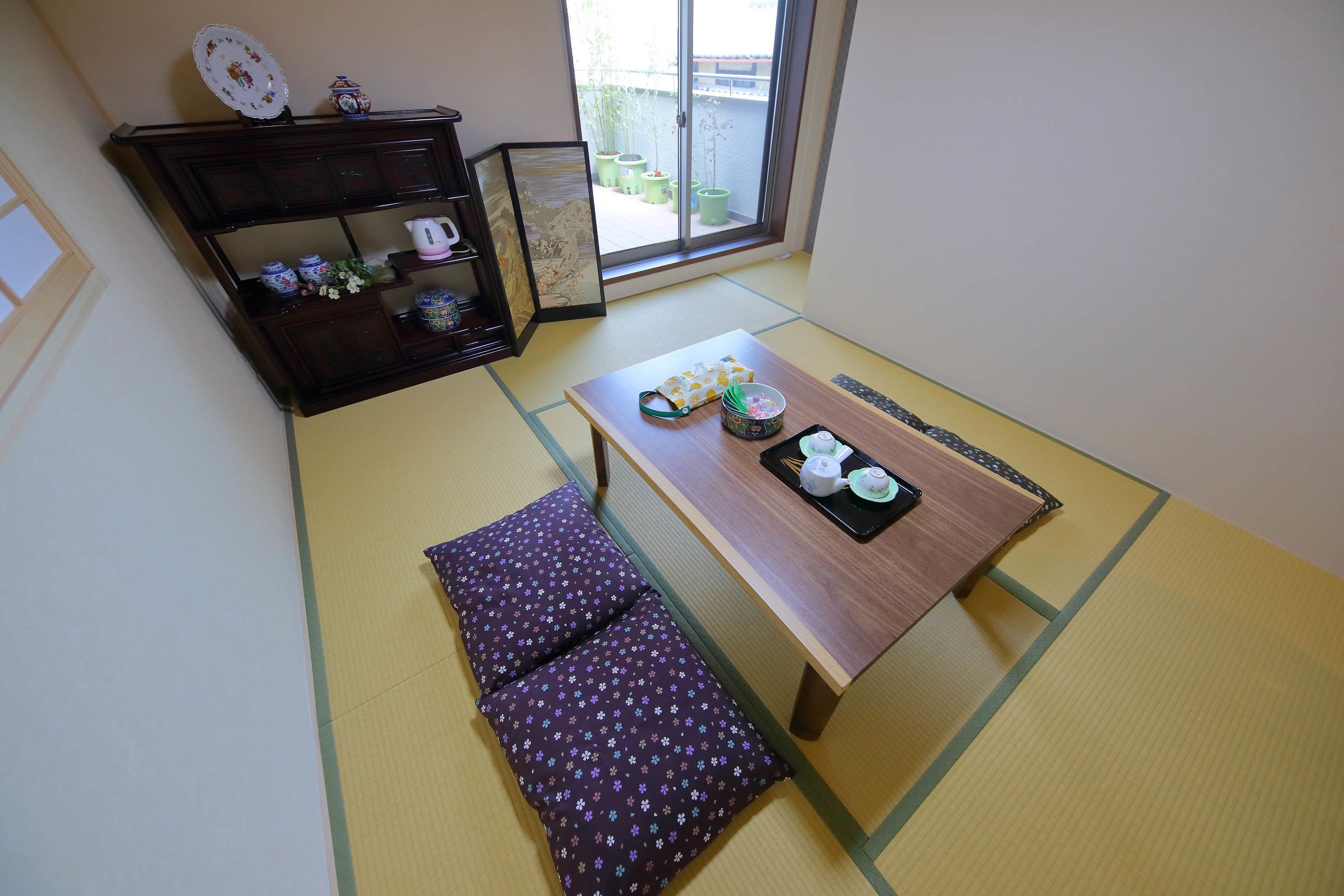 A traditional Japanese room with tatami flooring, a low table with a tea set, and a dark wooden cabinet with decorative items.