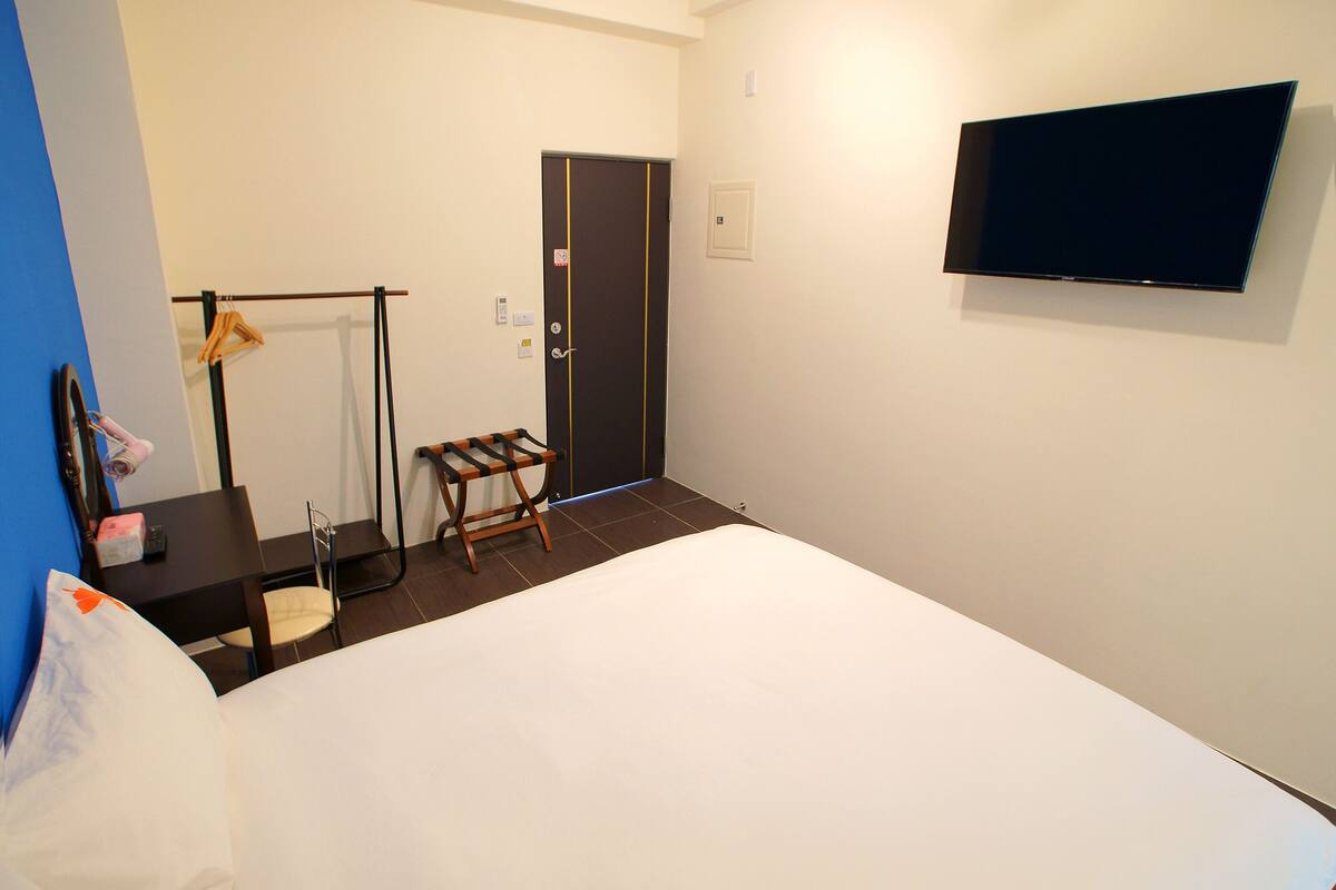 Een hotelkamer met een bed, een bureau met stoel, een aan de muur bevestigde televisie en een deur.