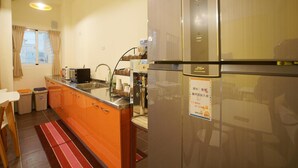 Een compacte keuken met een koelkast, een koffieapparaat en een klein eethoekje met stoelen.