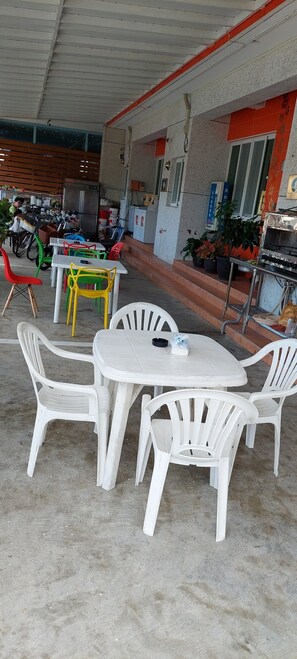 Un espace extérieur abrité, aménagé avec des chaises et des tables en plastique blanches et colorées.