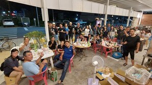 Een groep mensen zit rond tafels met eten en drinken, in een ruimte met uitzicht op de straat.