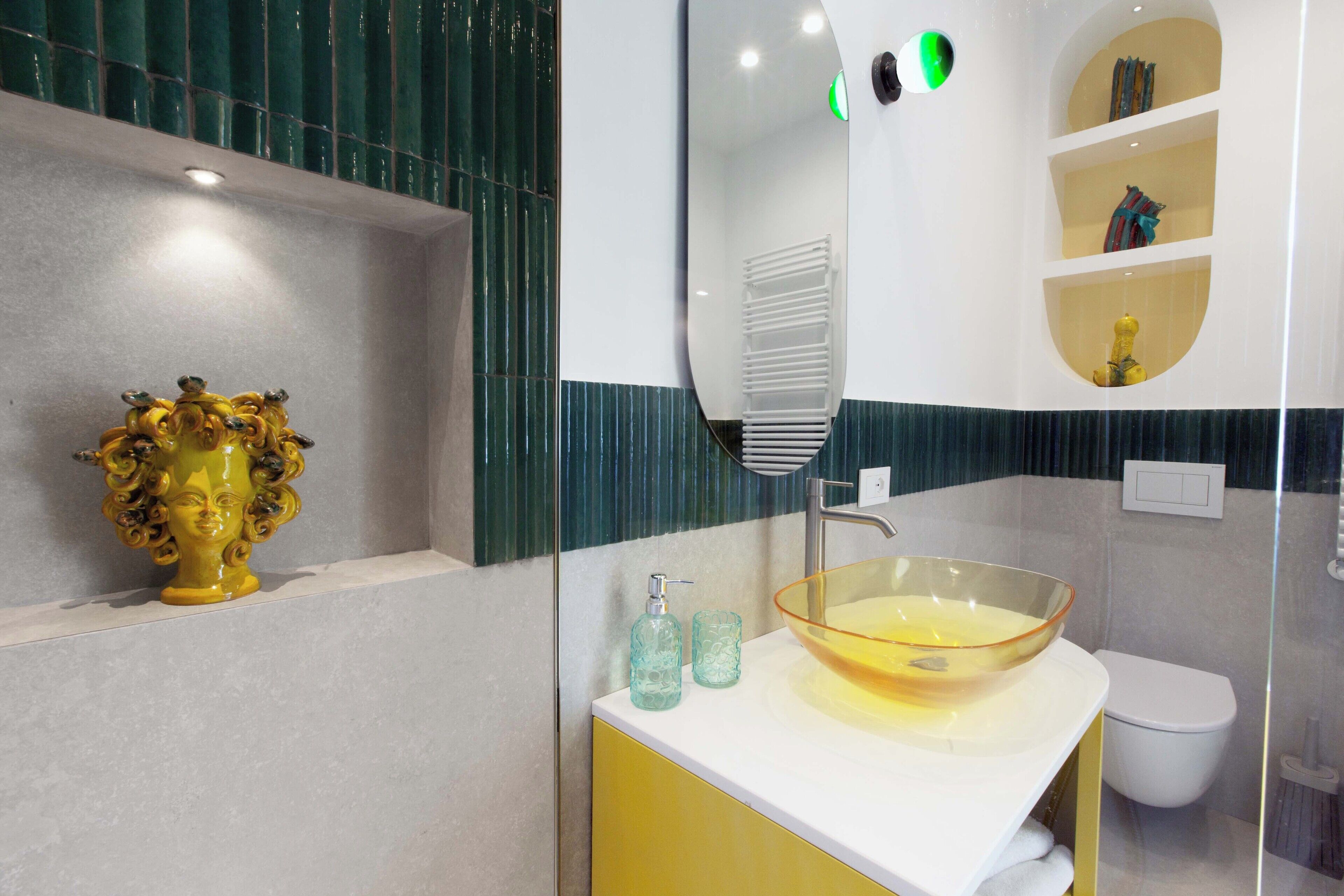 Un baño moderno con un tocador amarillo, un lavabo de vidrio y un inodoro blanco.