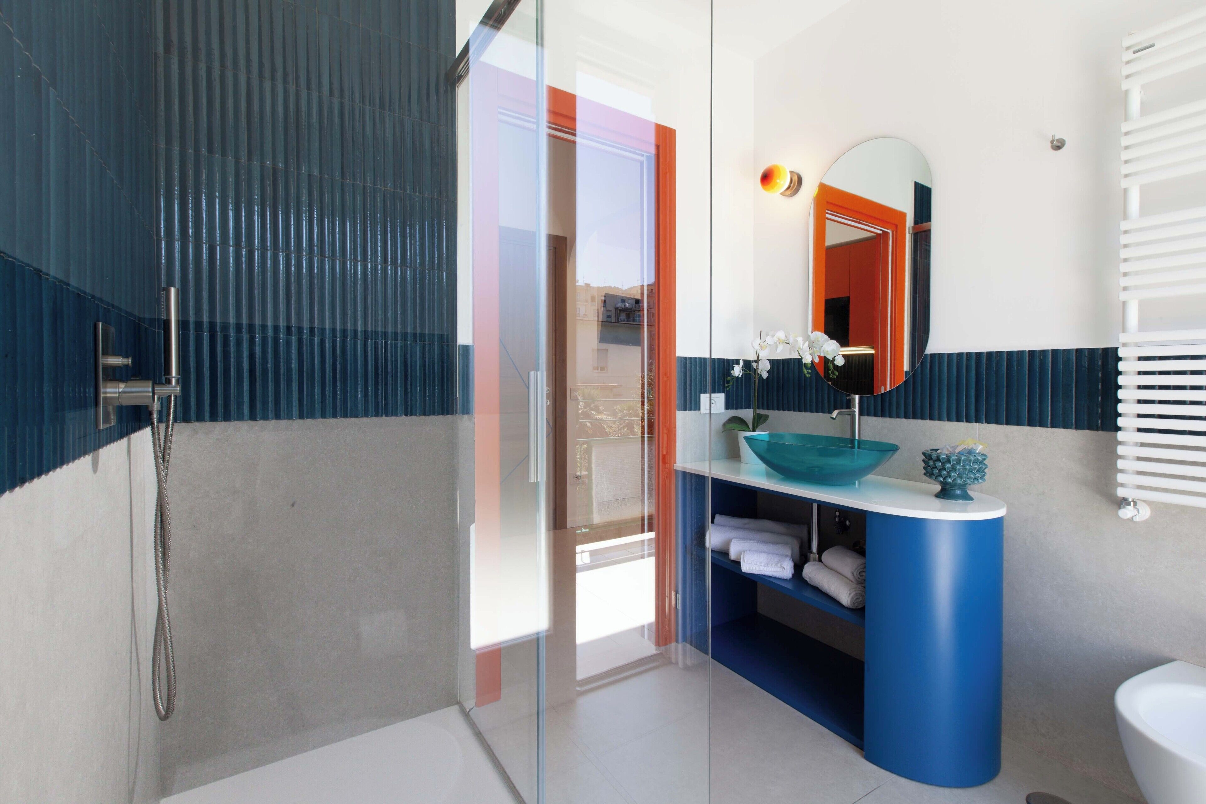 Un baño moderno con cabina de ducha de vidrio, un mueble de tocador azul con lavabo y un inodoro blanco.