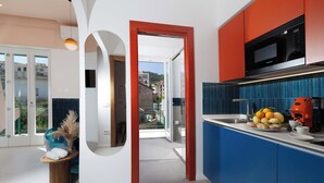 Une cuisine moderne avec un plan de travail bleu, une porte à cadre rouge et une vue sur la ville par la porte vitrée.