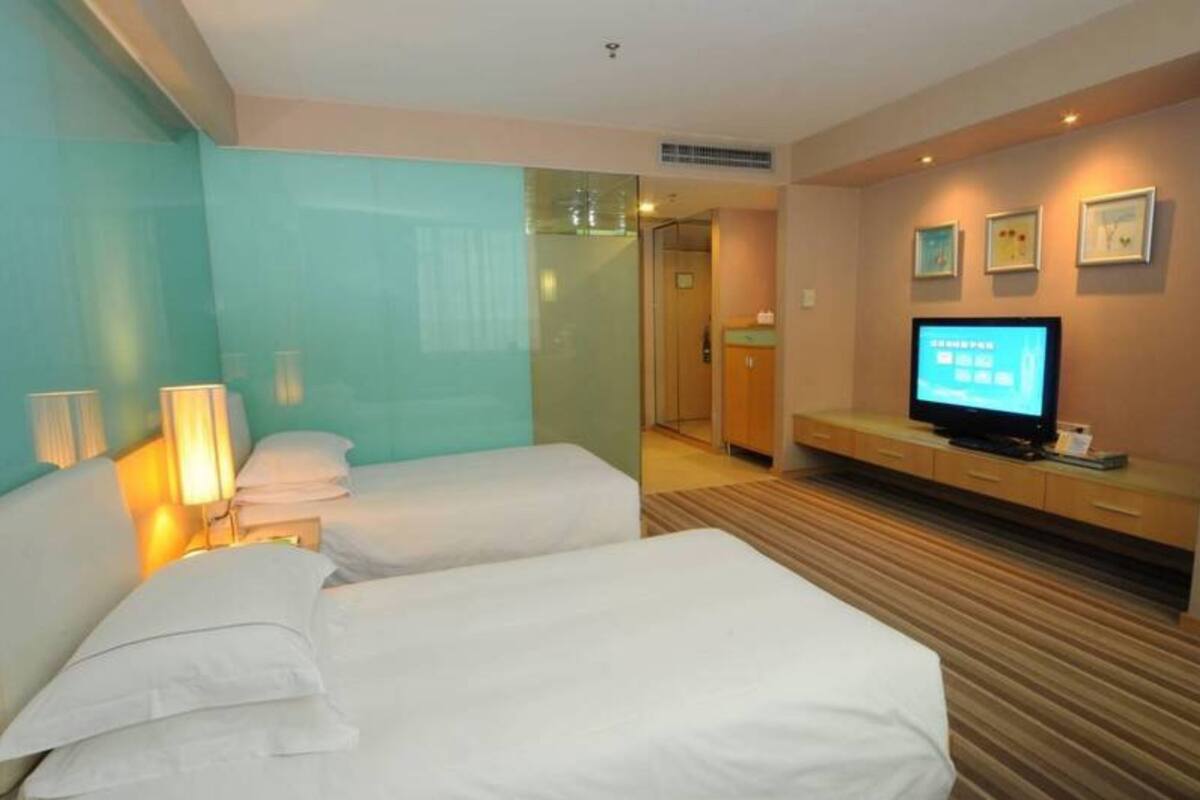 A hotel room with two beds, a television, and a bathroom visible through a glass door.