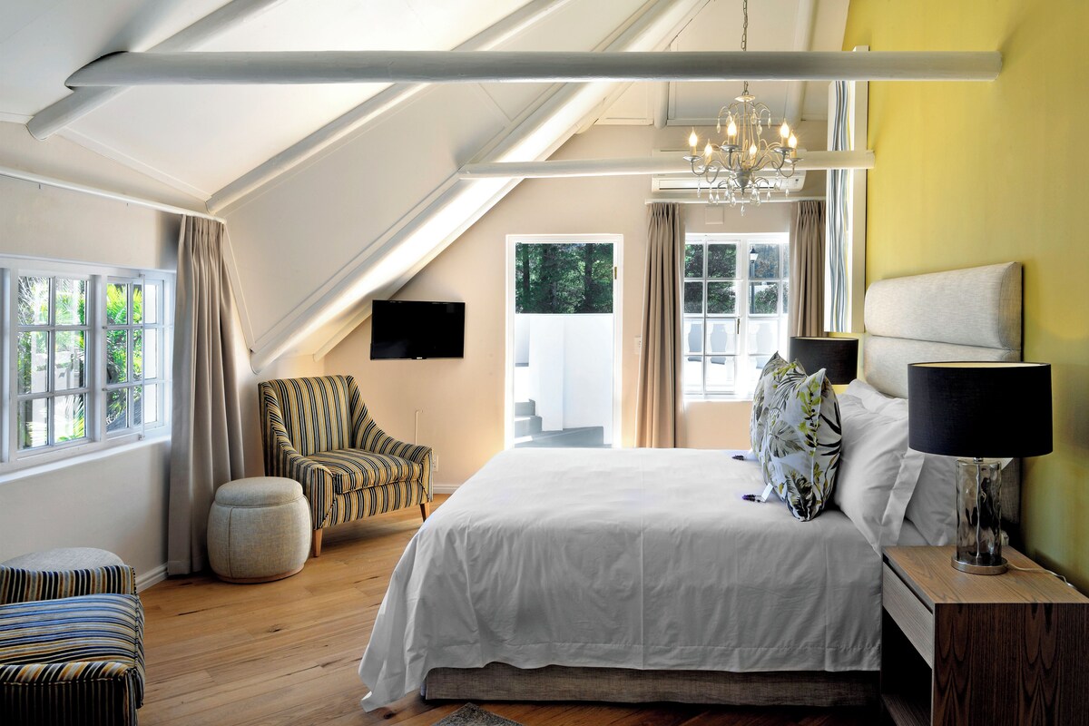Un dormitorio con una cama grande, una silla, un televisor, una lámpara y vistas al exterior.