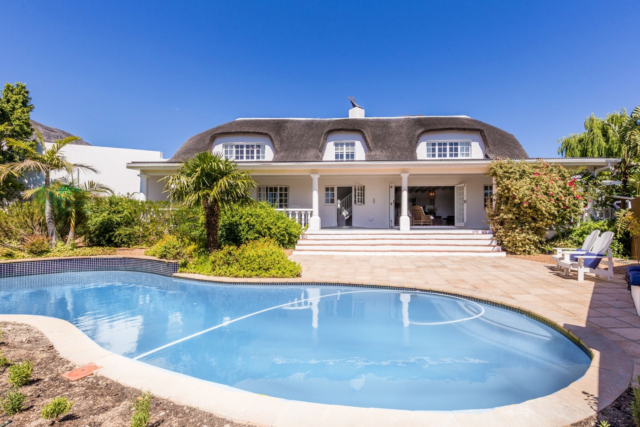 Una casa con piscina, un porche cubierto y un jardín bien cuidado.