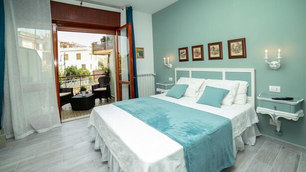 A bedroom with a bed, a nightstand, a window with curtains, and a view of the outside balcony. - Casa Minna (Sant'Agnello)