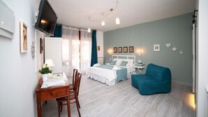 A bedroom with a bed, bedside tables, a desk with a chair, a blue armchair, and a TV mounted on the wall. - Casa Minna (Sant'Agnello)