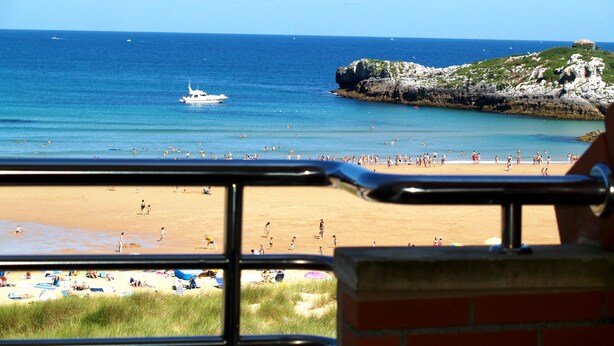 A beach with a view of the ocean, a boat, and rocky cliffs. - Apartamentos Marítimo Ris (Noja)