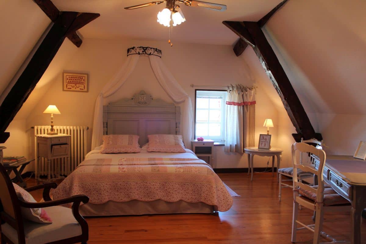 Une chambre à coucher avec un grand lit, un ventilateur de plafond, une fenêtre avec des rideaux et un radiateur.