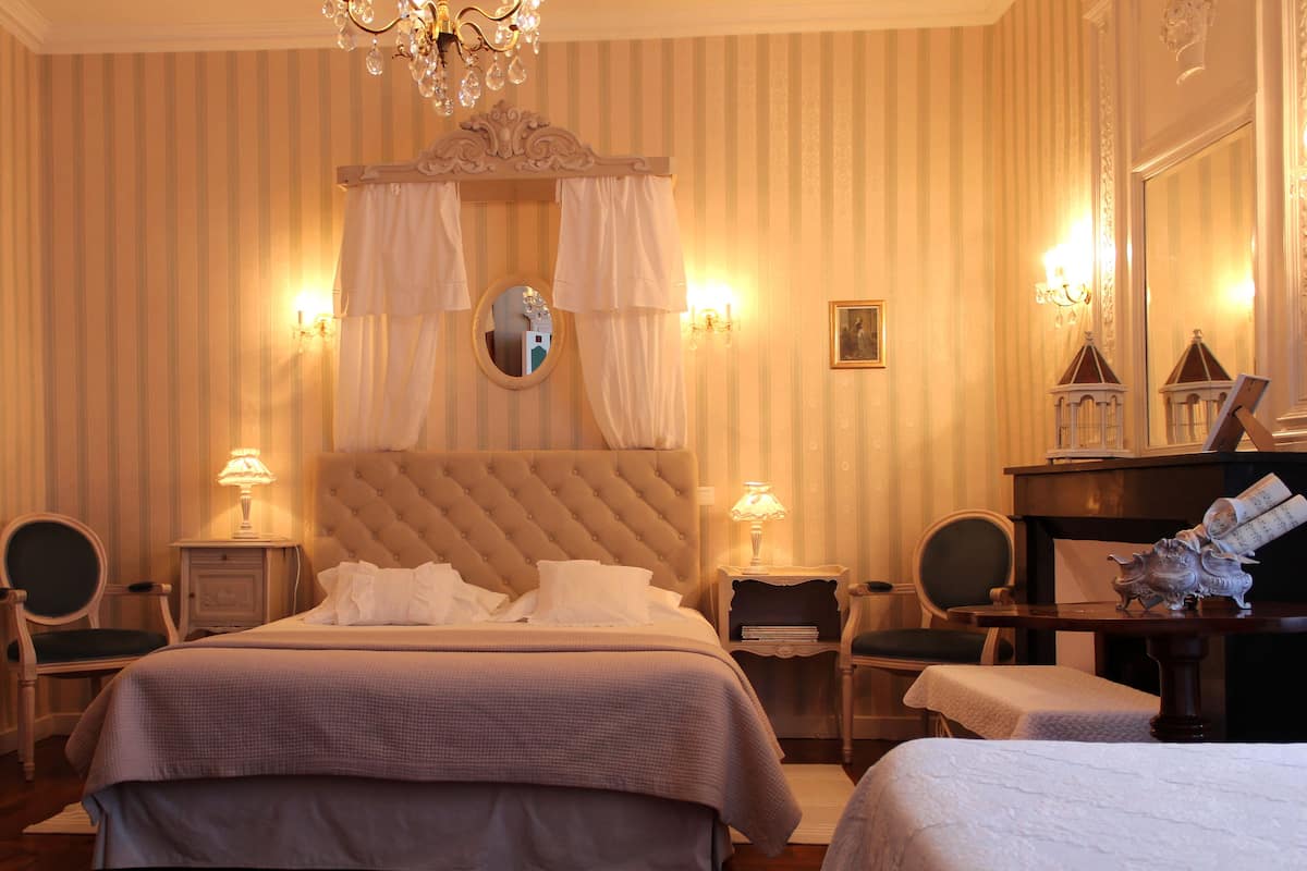 Une chambre d’hôtel avec un grand lit, deux tables de chevet, une chaise, une petite table et un miroir décoratif.