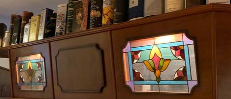 Een houten kast met diverse flesjes drank en een glas-in-loodraam.