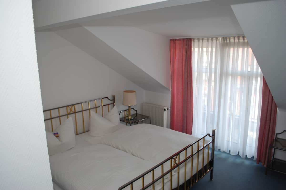A bedroom with a bed, a nightstand, a lamp, and a window with curtains.