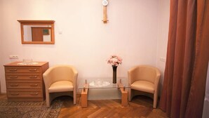 A room with a wooden dresser, two chairs, a glass coffee table, a vase with flowers, a wall clock, and a mirror. - Apartamenty Kazimierz (Kraków)