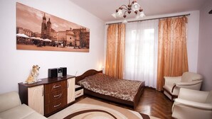 A bedroom with a bed, a desk, a chair, a sofa, a large painting, and a chandelier. - Apartamenty Kazimierz (Kraków)