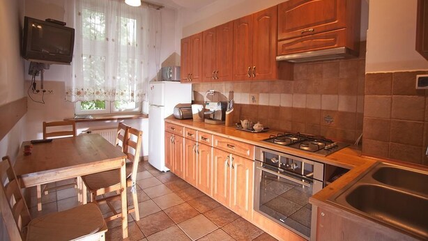 A kitchen with wooden cabinets, a gas stove, a sink, and a dining area with chairs and a table. - Apartamenty Kazimierz (Kraków)