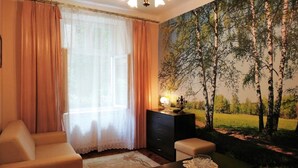 A room with a large window, a painting of trees, a dresser, and a chair. - Apartamenty Kazimierz (Kraków)