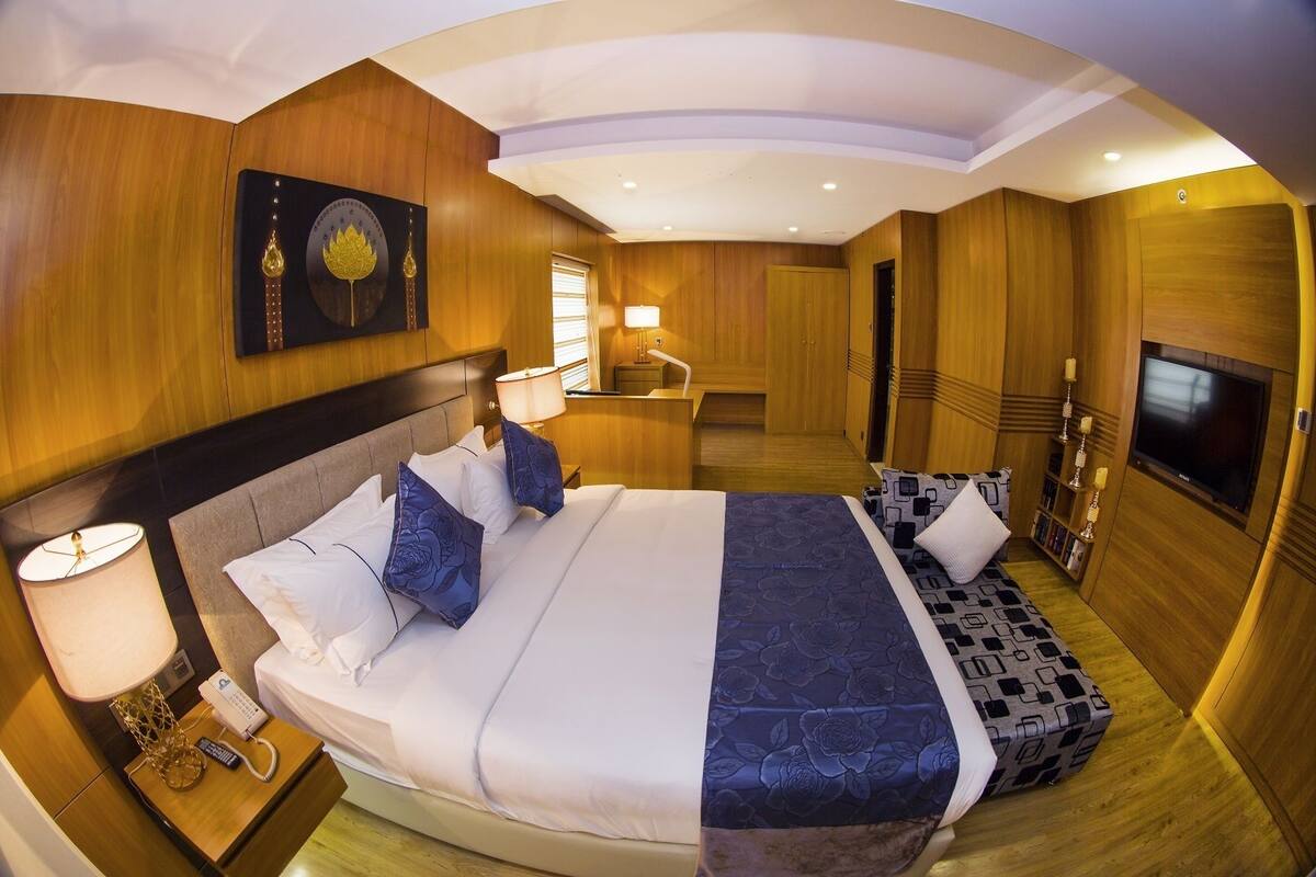 A modern hotel room with a large bed, bedside lamps, a TV, and a wooden interior.