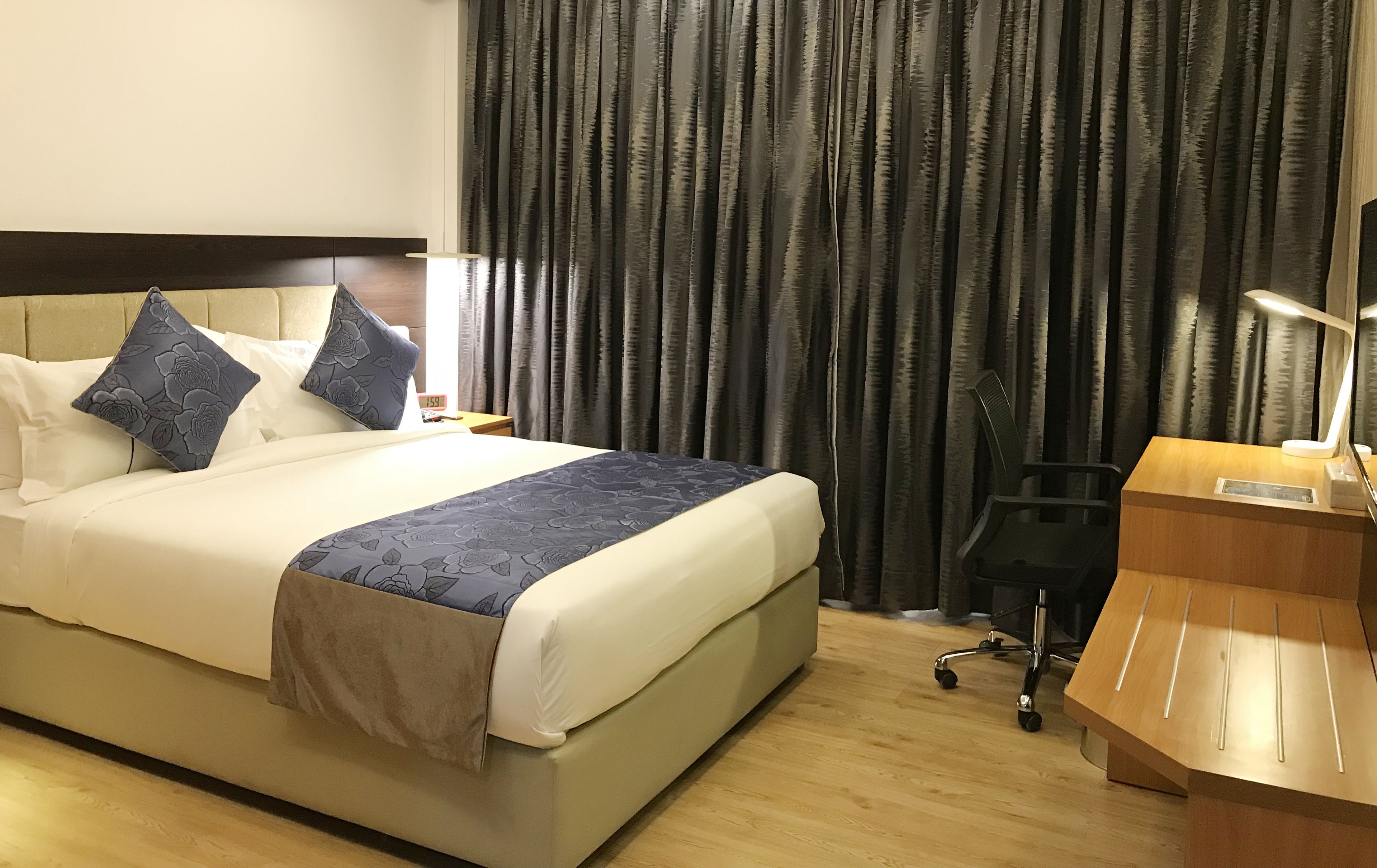 Ein Hotelzimmer mit Bett, Schreibtisch, Stuhl und einem großen Fenster mit Vorhängen.