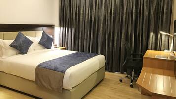 Ein Hotelzimmer mit Bett, Schreibtisch, Stuhl und einem großen Fenster mit Vorhängen.