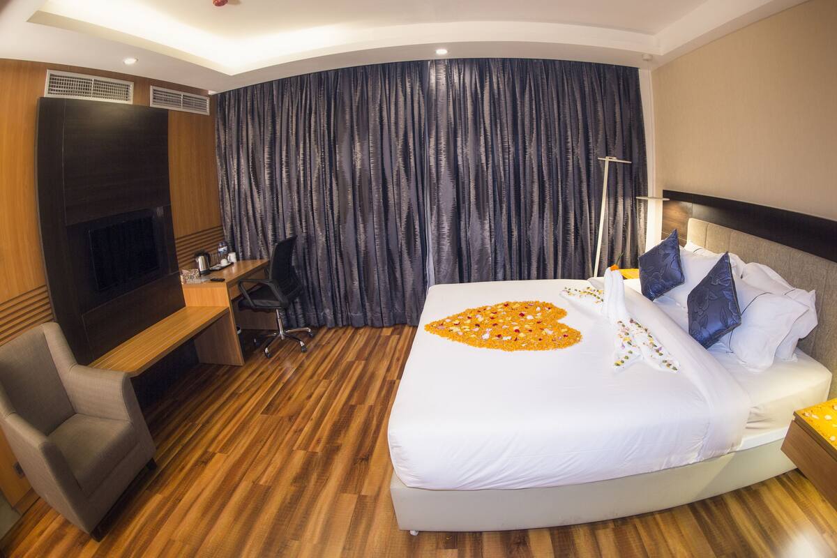 A hotel room with a large bed, a desk, a chair, a TV, and a curtain.