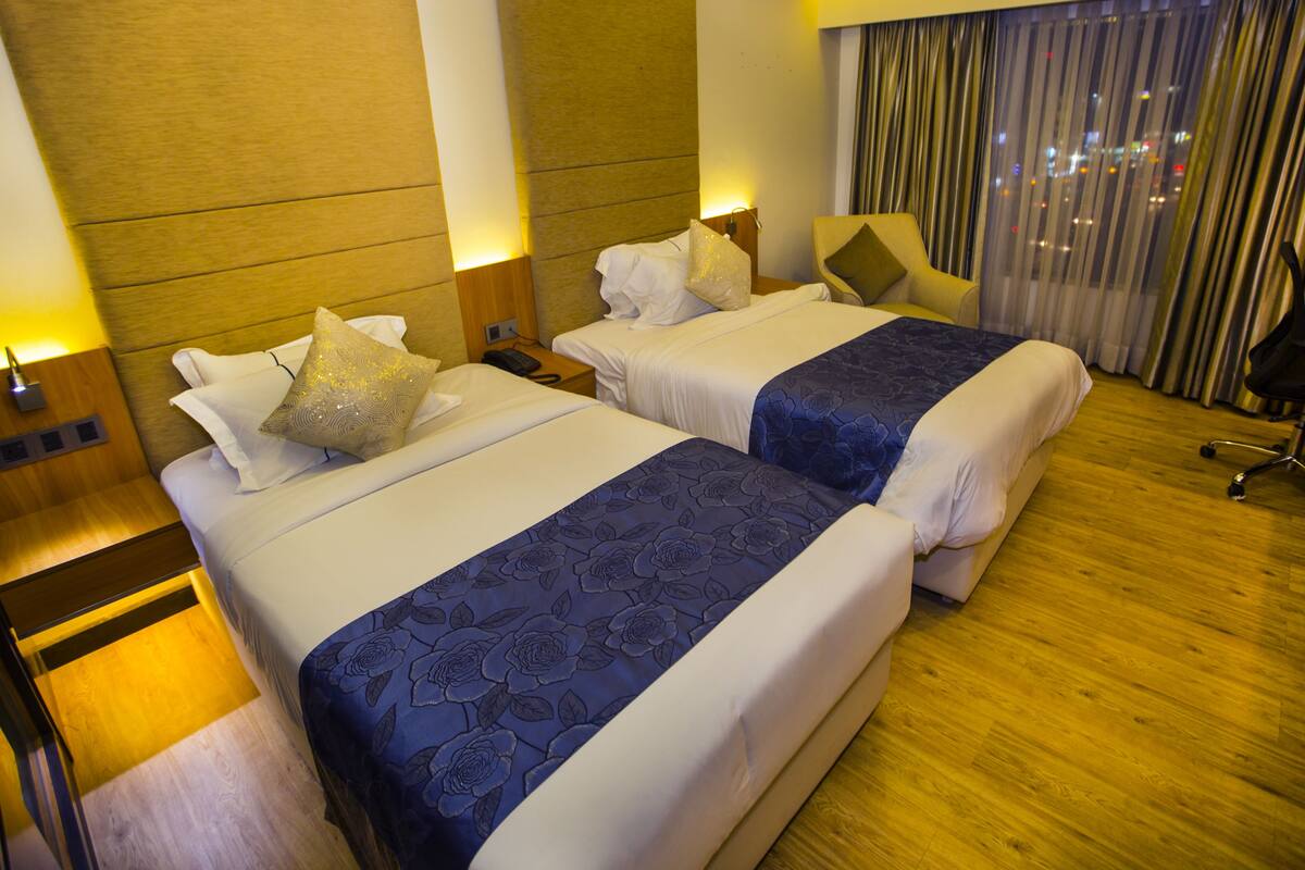 A hotel room with two beds, wooden flooring, a desk, and a chair.