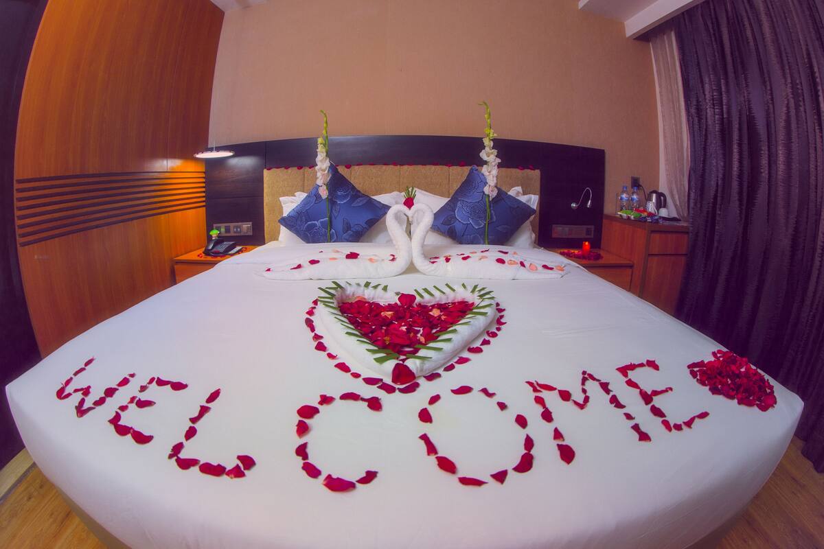 A bed with a heart-shaped arrangement of rose petals and a "WELCOME" message.