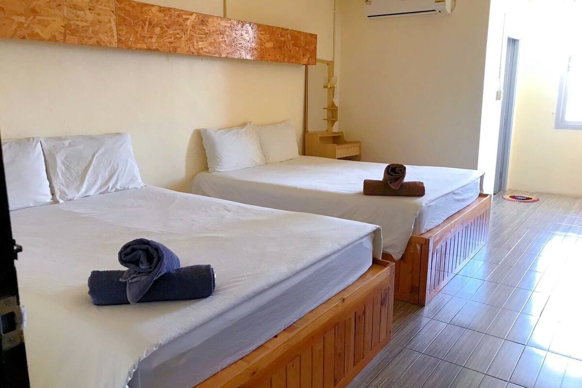 A hotel room with two beds, wooden headboards, white bedding, and a wooden floor.