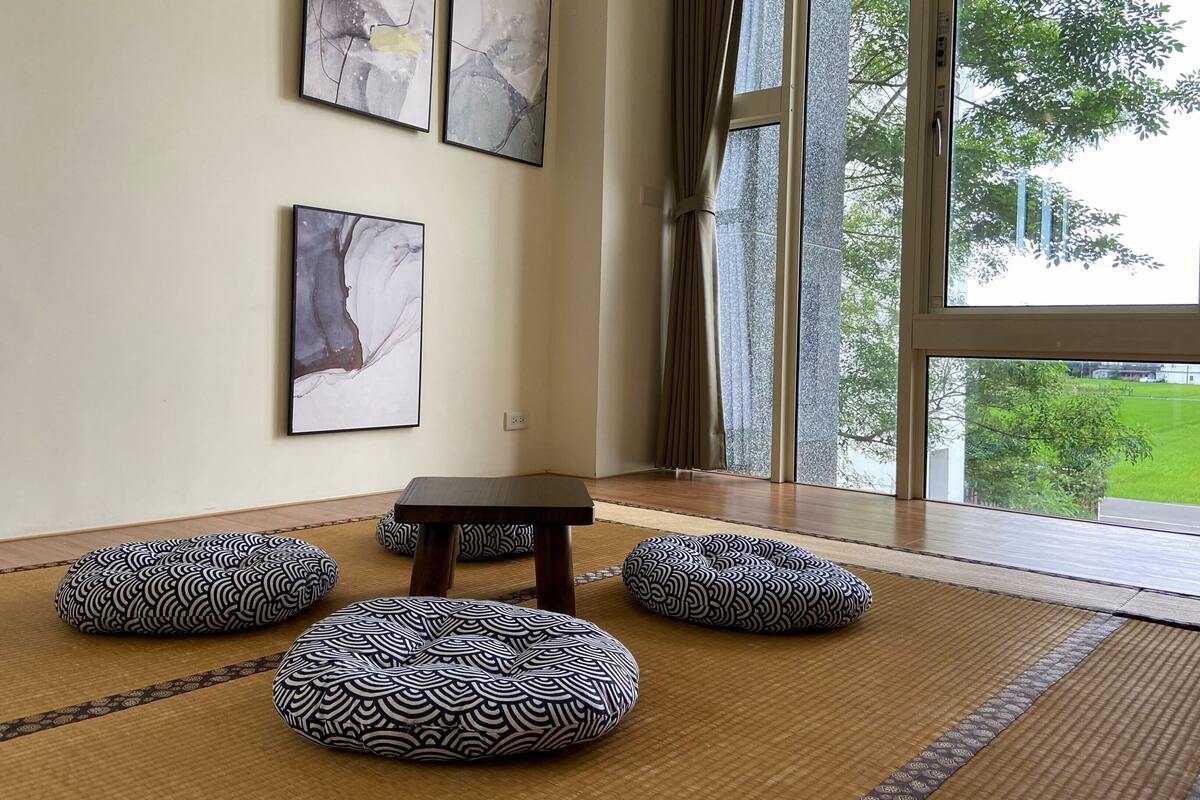 A room with tatami mats, a small table, and three cushions. There are four abstract paintings on the wall.