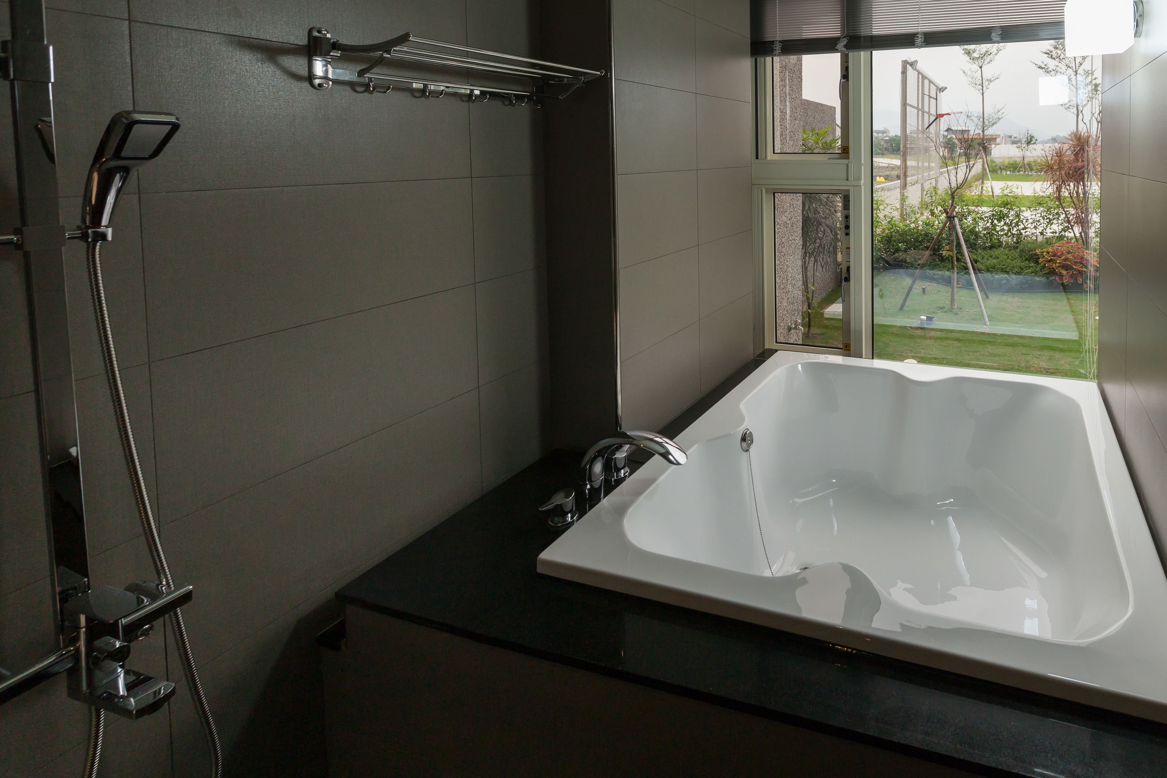 A modern bathroom with a large bathtub, a shower, and a window offering a view of a garden.