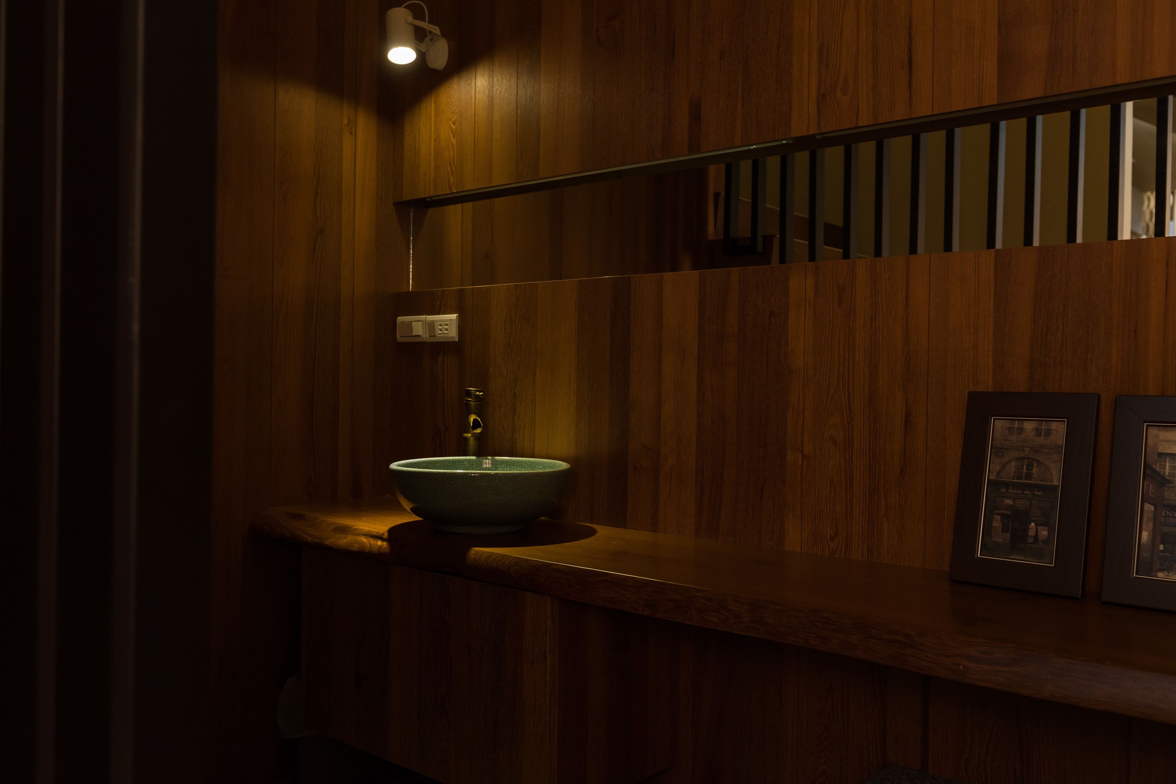 A wooden bathroom with a vessel sink, a mirror, and framed pictures on the wall.
