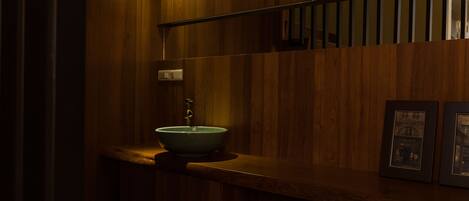 A wooden bathroom with a vessel sink, a mirror, and framed pictures on the wall.