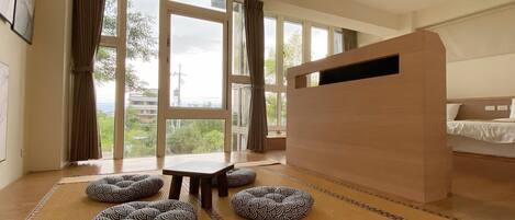 A room with tatami mats, a low wooden desk, and a bed with a headboard.