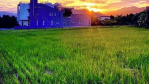 Un edificio moderno con techo plano y varias ventanas, ubicado en un campo verde con un atardecer de fondo.