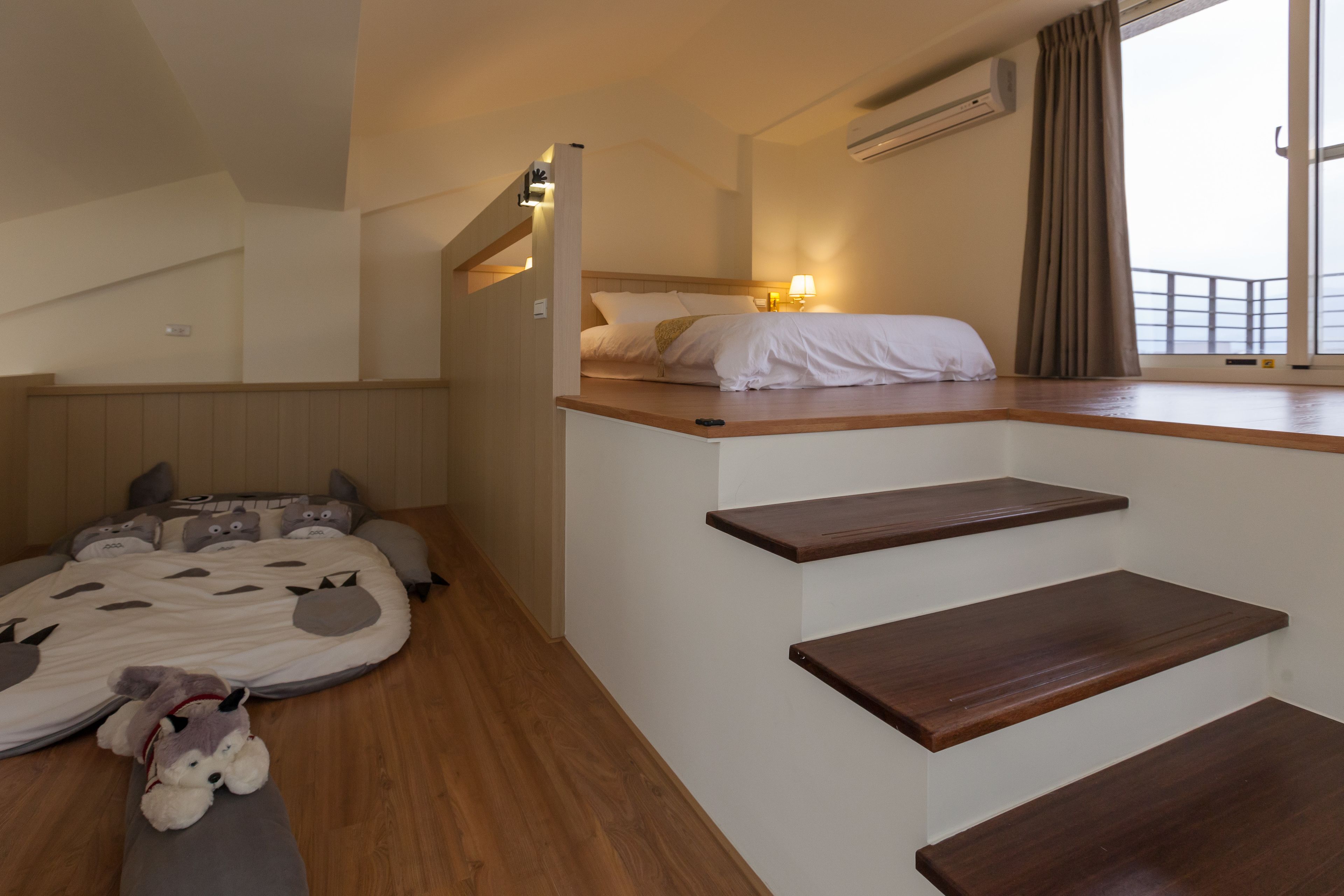 Un dormitorio con cama, ventana con cortinas, una escalera y un peluche en el suelo.